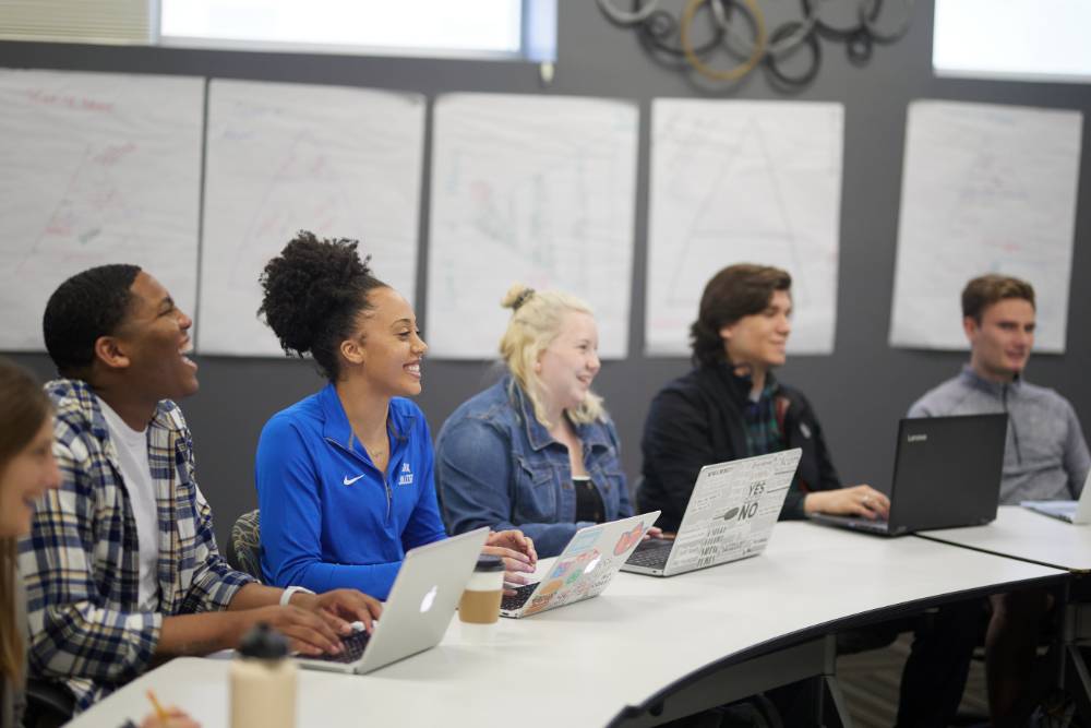 group of students sitting at table with laptops